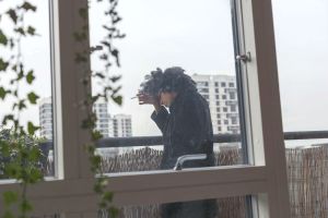 Eine Person steht am Balkon und greift sich wärend dem Rauchen auf die Stirn, symbolisch für Appetitlosigkeit durch Liebeskummer