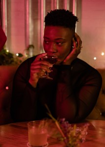 A non-binary person sipping a drink at a bar