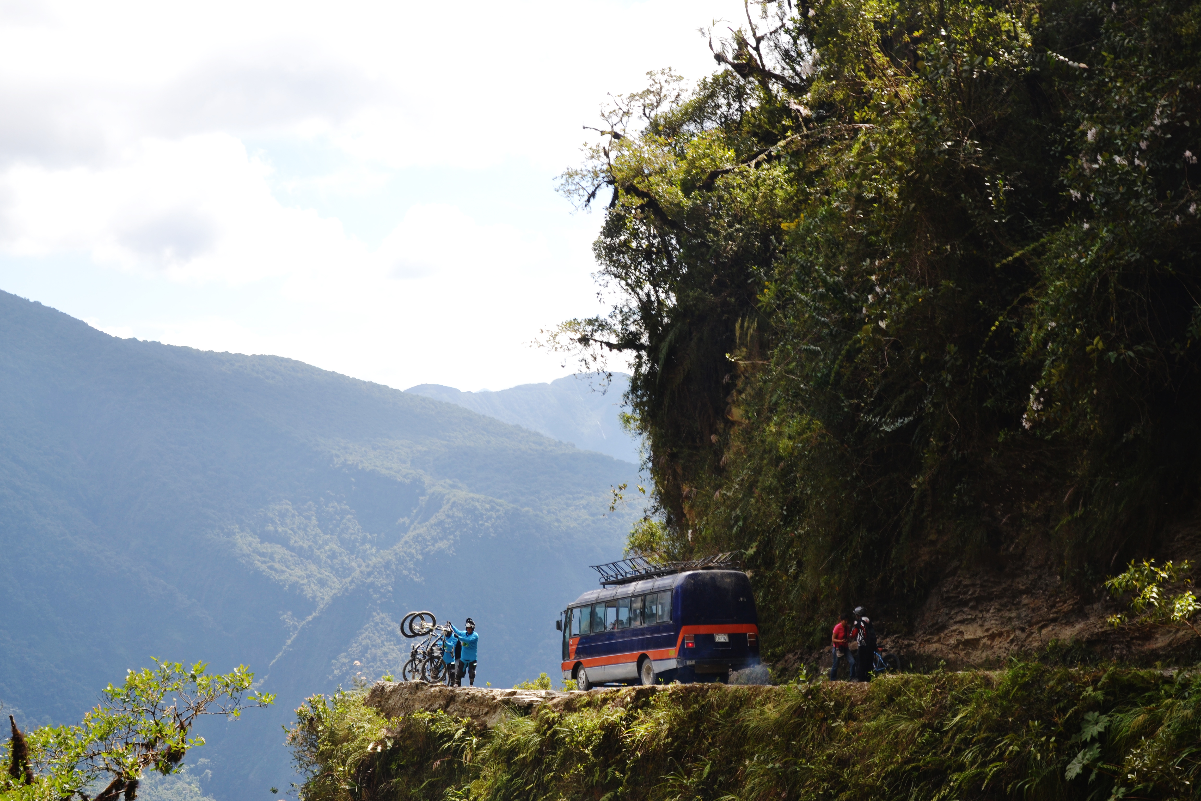 Ein Bus kurvt um die Ecke vor der vier Mountainbiker ihre Räder in die Höhe recken