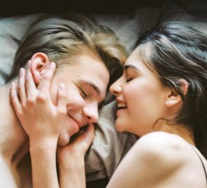 Ein heterosexuelles Pärchen liegt glücklich im Bett und lacht