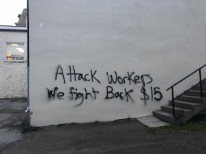 A white wall spray painted with Attack Workers We Fight Back $15.