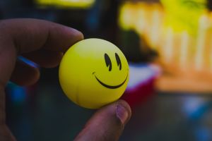 Fingers pinching a yellow ping pong ball with a smiley face on it