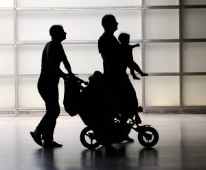 Eine Mutter schiebt den Kinderwagen, der Vater trägt ein Kleinkind.