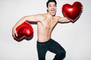 Hombre joven, sin camisa, sosteniendo un par de globos en forma de corazón.