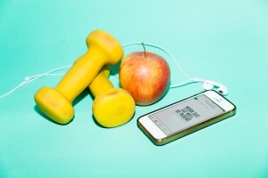 Gelbe Hanteln liegen neben einem Apfel und Handy mit Kopfhörern und Motivationsspruch