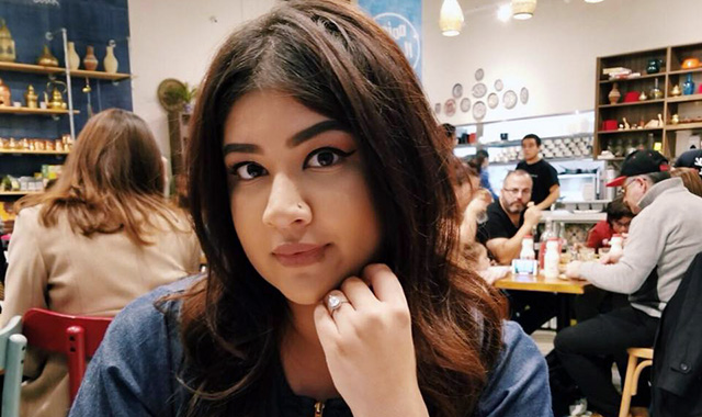 Eine junge Frau mit braunen Haaren sitzt in einem Restaurant und schaut direkt in die Kamera