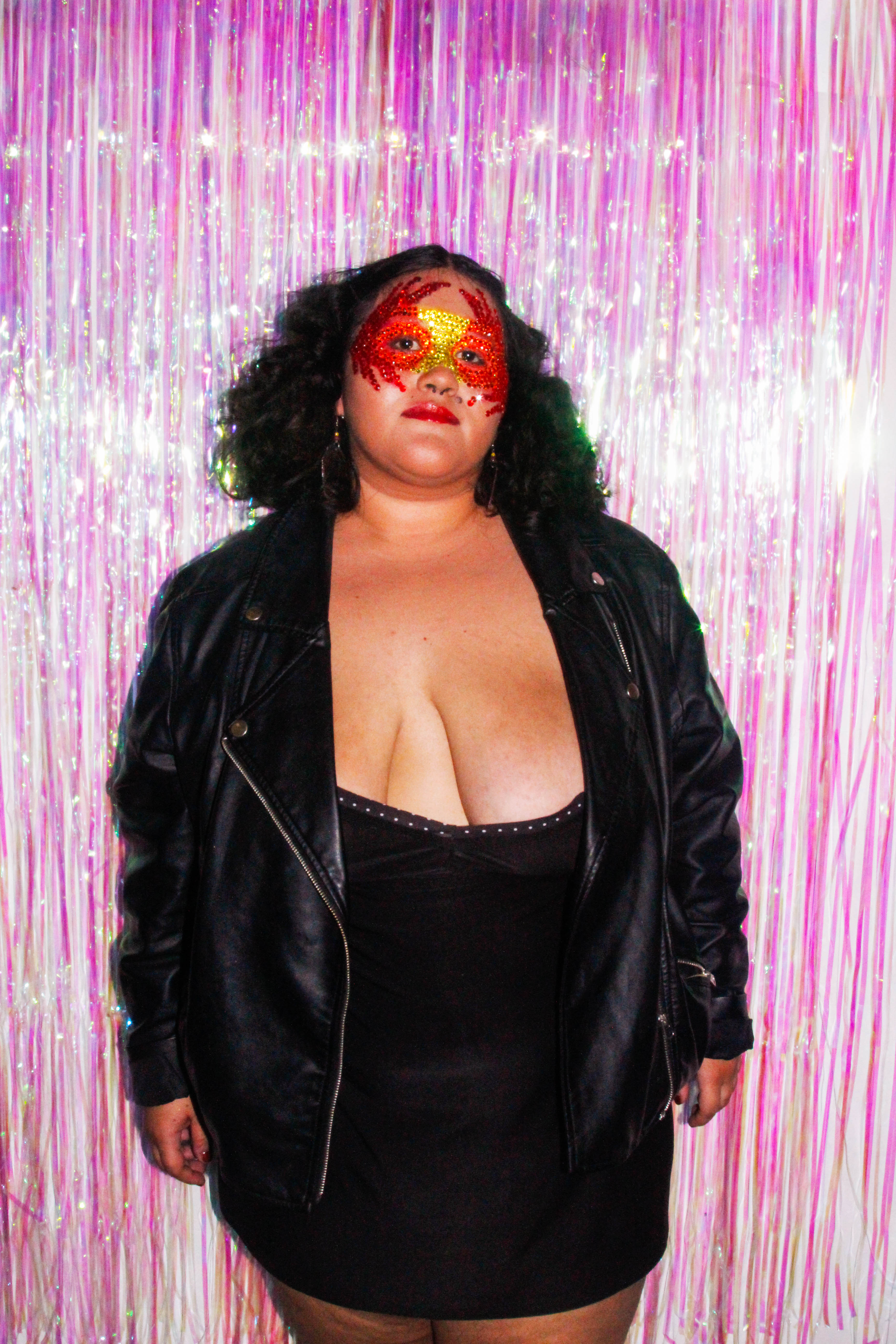 A woman in a mask standing in front of a pink curtain