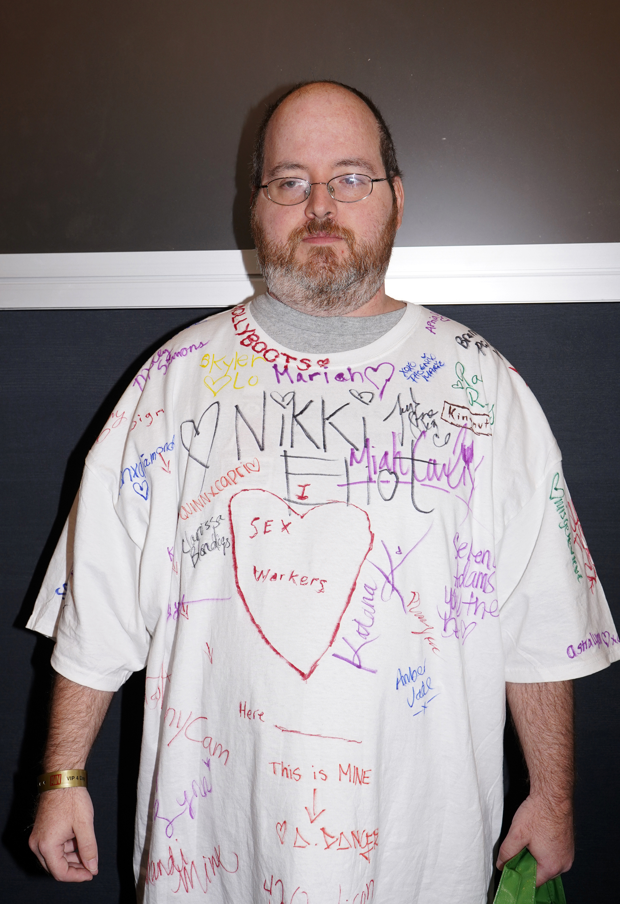 A man wearing a T shirt covered in the signatures of porn actors and cam models