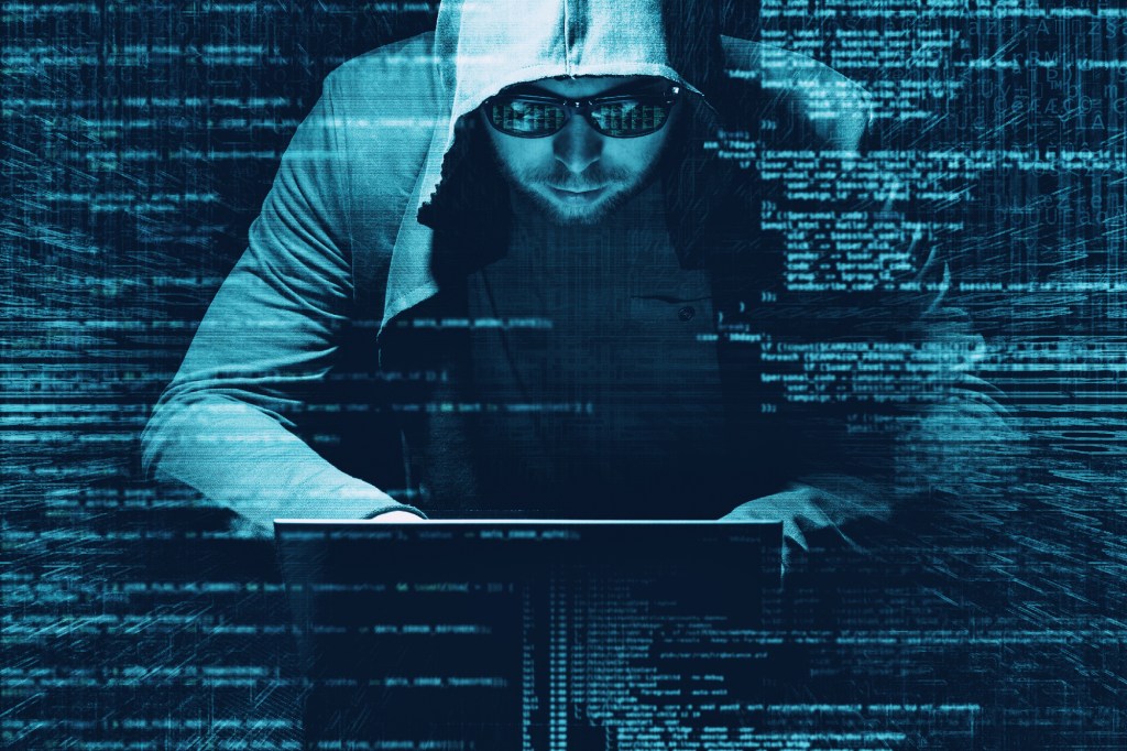 A blue tinted image of a man wearing a hoodie and glasses slouching over a laptop, with superimposed lines of code around the image