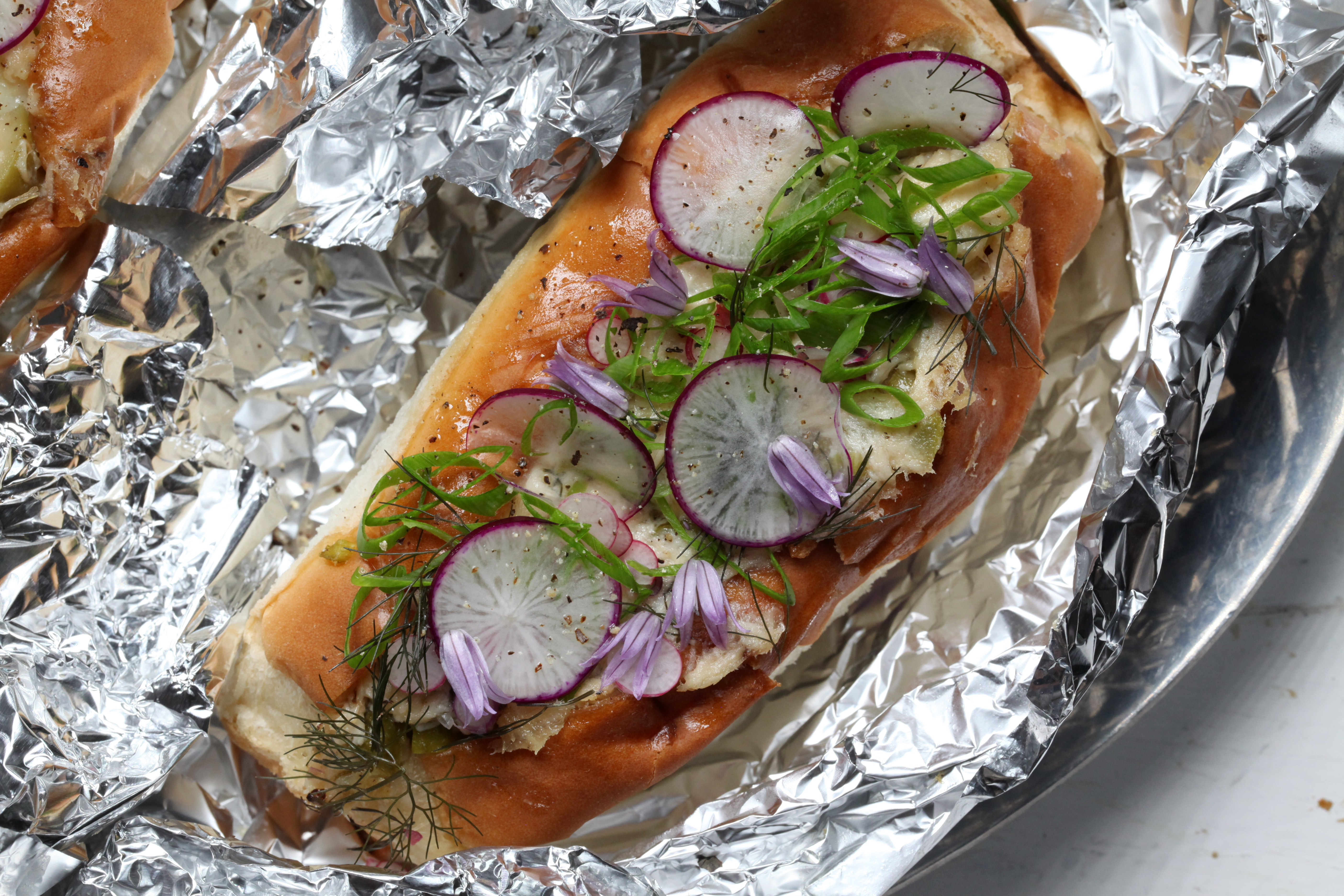 a tuna melt topped with radishes, green onions, and chive blossoms and made by chef erik anderson of coi in san francisco