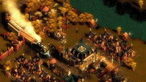 A train pulls into a town through a grove of autumn-colored trees.