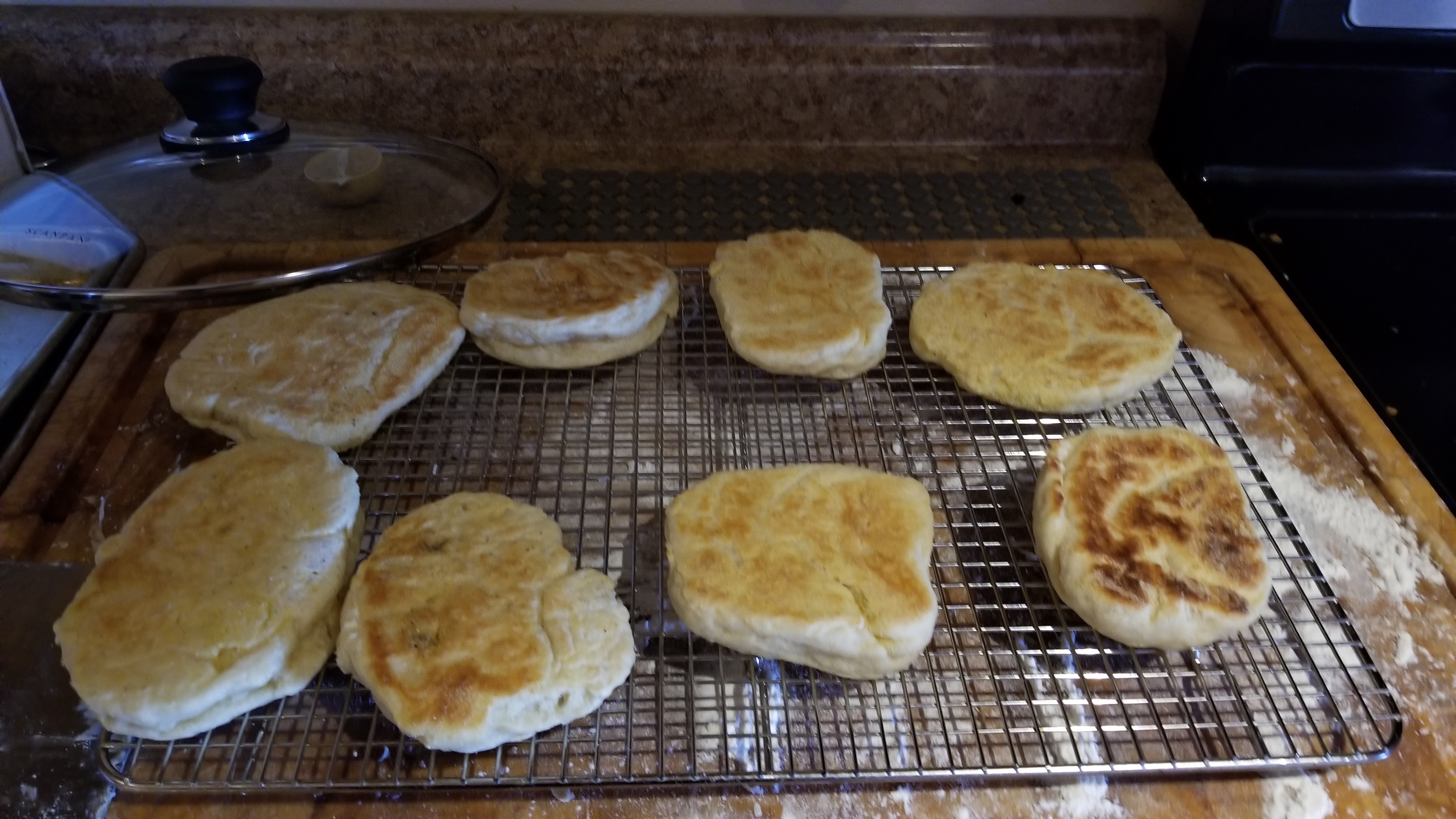 a photo of a series of flat failed english muffins on a cooling rack.