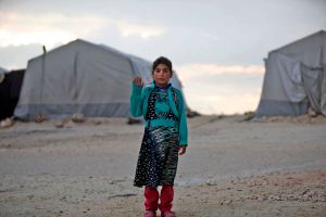 A young girl in a refugee camp waves to the camera.