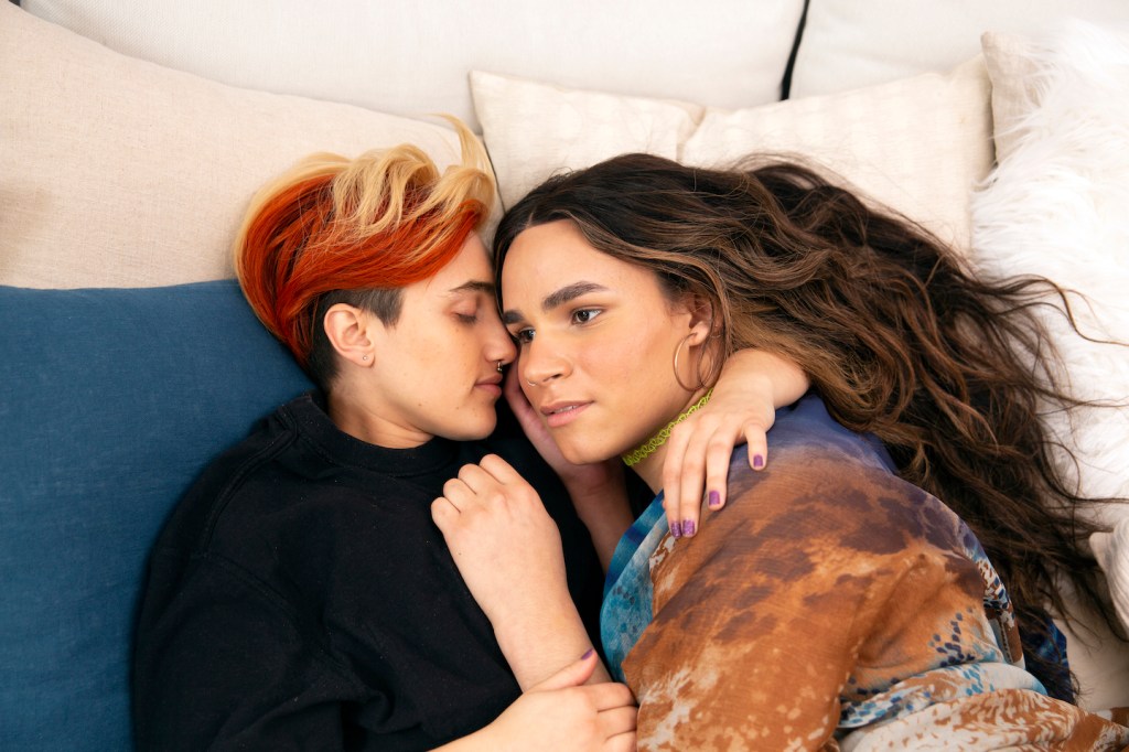A transmasculine gender-nonconforming person and transfeminine non-binary person waking up together in bed