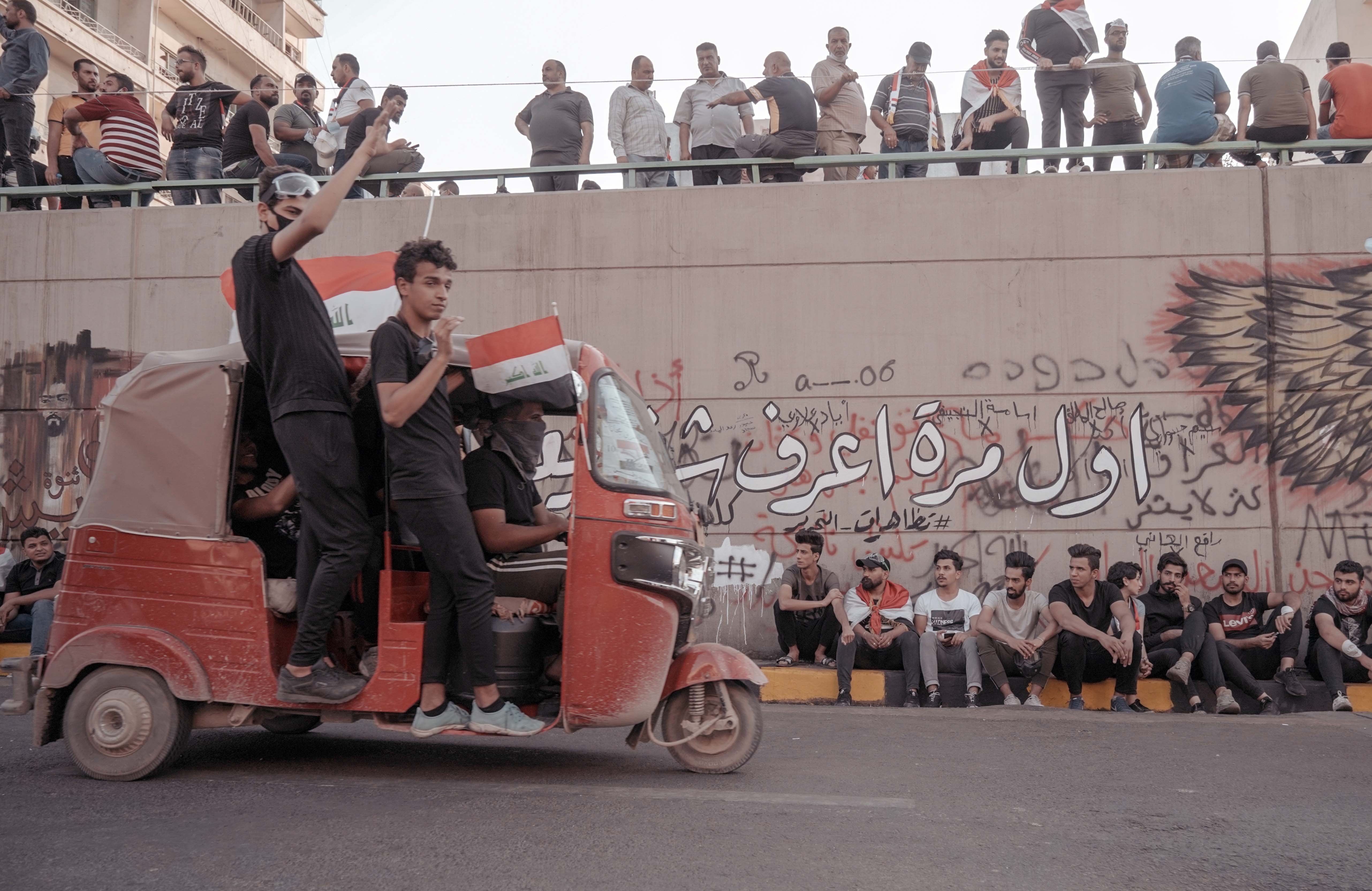 Young men hanging out of a tuk-tuk during the demonstrations in Baghdad, Iraq