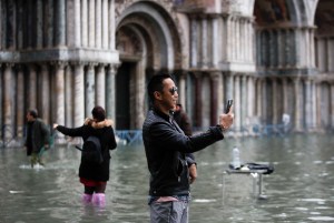 Tourists take pictures in a flooded St. Mark's Square, in Venice, Wednesday, Nov. 13, 2019.