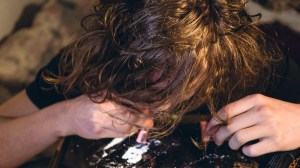 Ein Mann mit langen Haaren zieht Kokain durch einen Geldschein