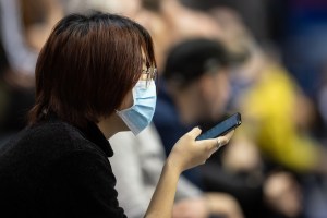A spectator wears a mouthguard and holds her smartphone in her hand at a table tennis tournament in Germany. (Photo: Swen Pförtner/picture alliance via Getty Images)​