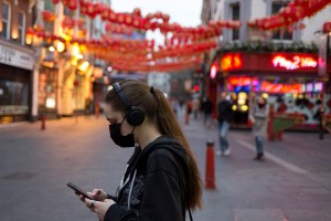 A masked young woman stands in Chinatown, on 18th March 2020, in London, England.