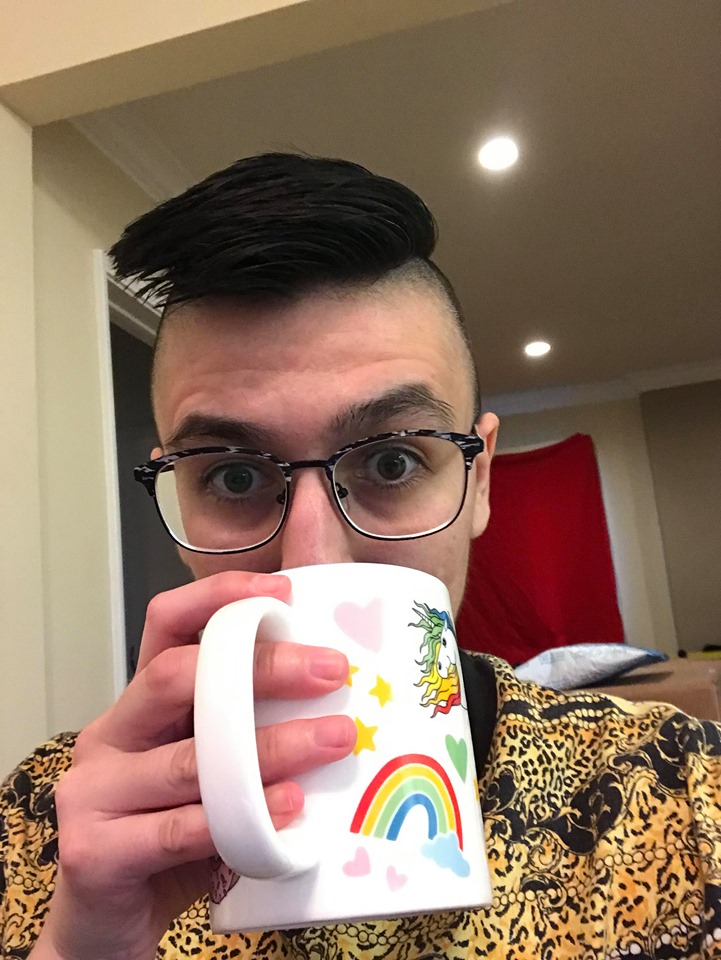 image of person with short haircut and sides of head shaved drinking from rainbow mug