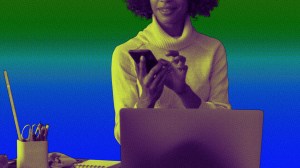 Een vrouw zit op haar telefoon achter haar laptop