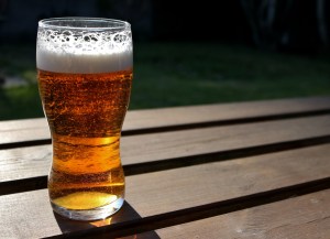 a glass pint of light beer on top of a wooden picnic table