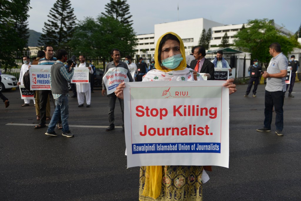 Perempuan berhijab dan bermasker memegang poster bertuliskan "Stop Killing Journalist"