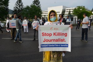 Perempuan berhijab dan bermasker memegang poster bertuliskan "Stop Killing Journalist"