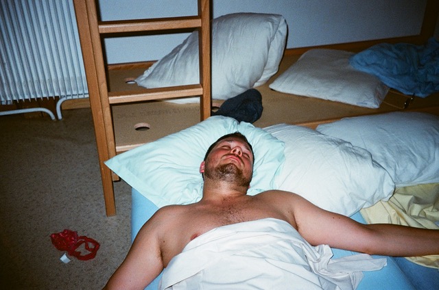 Shirtless guy passed out on a mattrass with his arms open wide and a pair of female panties on the floor.