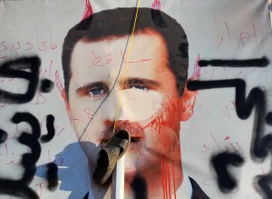 A slipper hangs on a vandalised poster of Syrian President Bashar al-Assad lying in a trash container in the northern city of Aleppo on July 24, 2012.