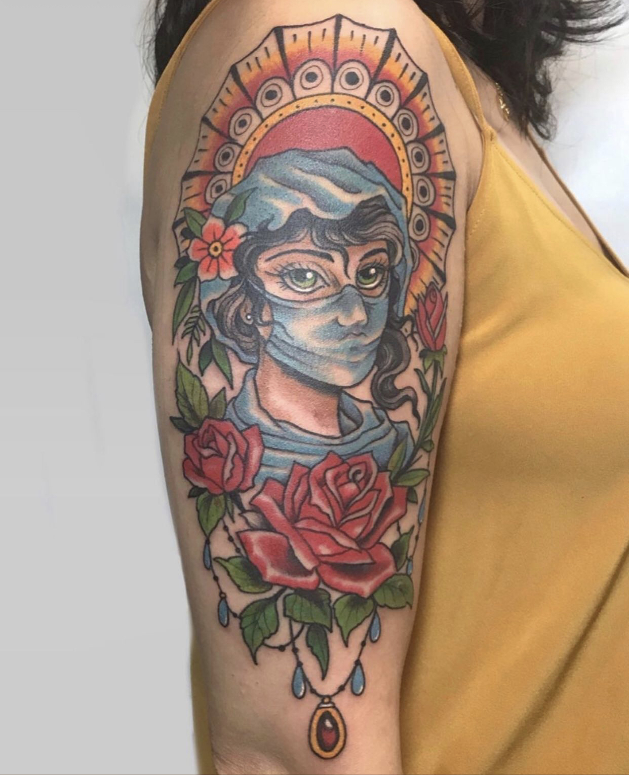 Das Tattoo zeigt eine Krankenschwester mit Mund-Nasen-Schutz und verschiedenen Blumen als Verzierung