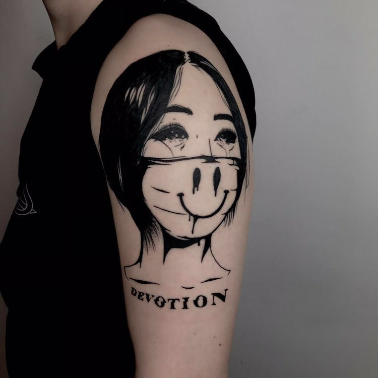 Das Tattoo zeigt eine junge, weinende Frau mit Mund-Nasen-Schutz, unter ihr steht das Wort