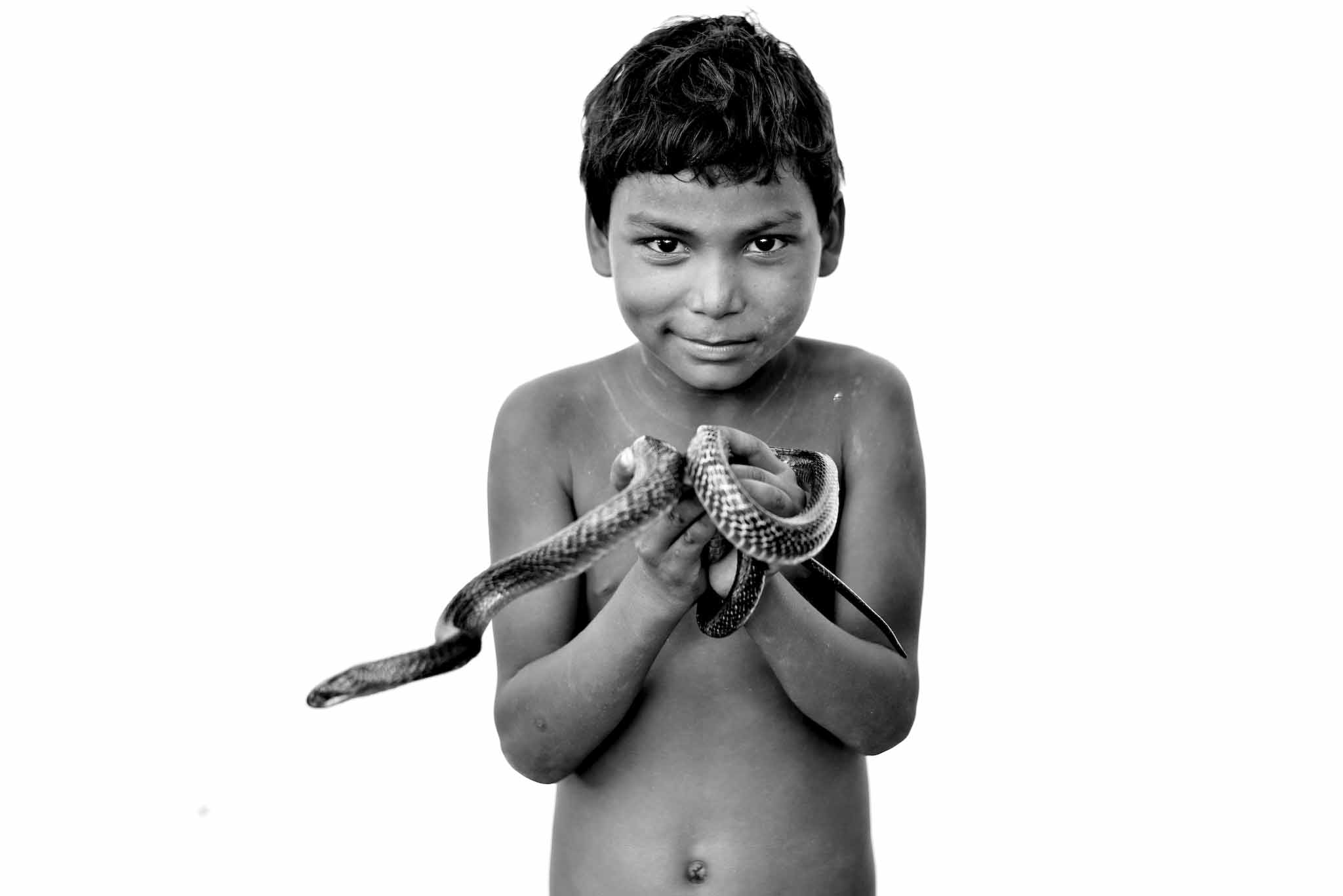 Dinesh Nath, 8 tahun, berpose dengan ular. Kakeknya Dinesh masih menerima panggilan untuk tampil dalam acara tertutup. Foto oleh Arun Sharma.