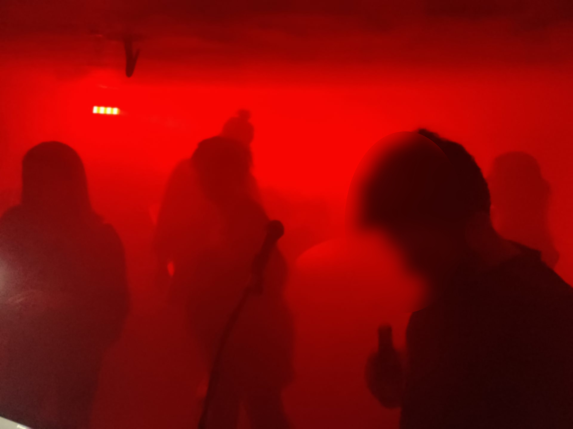 Ein rot beleuchteter, nebliger Raum, in dem die Umrisse tanzender Menschen zu sehen sind