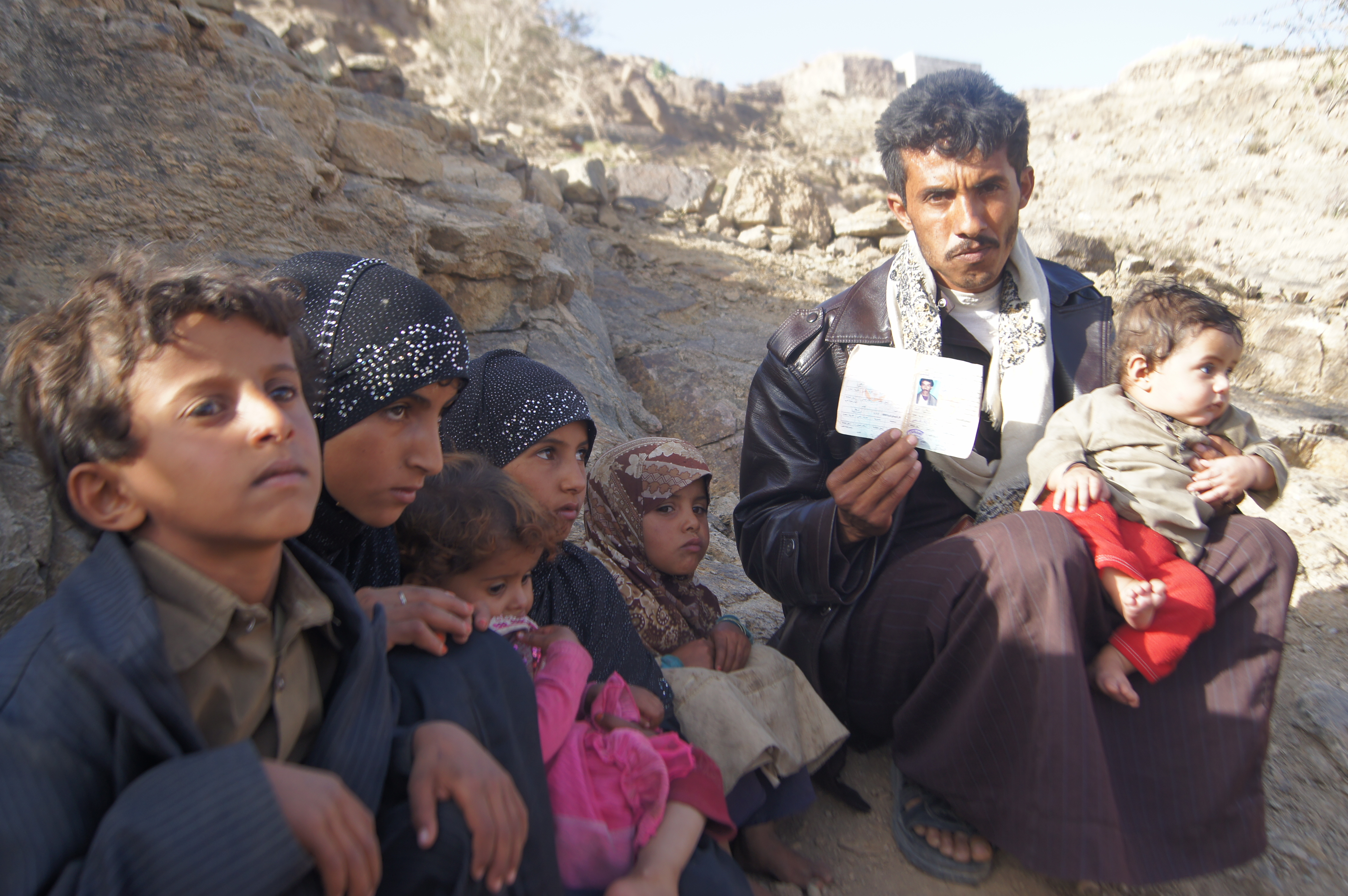 A man sits with six children while holding a photograph.
