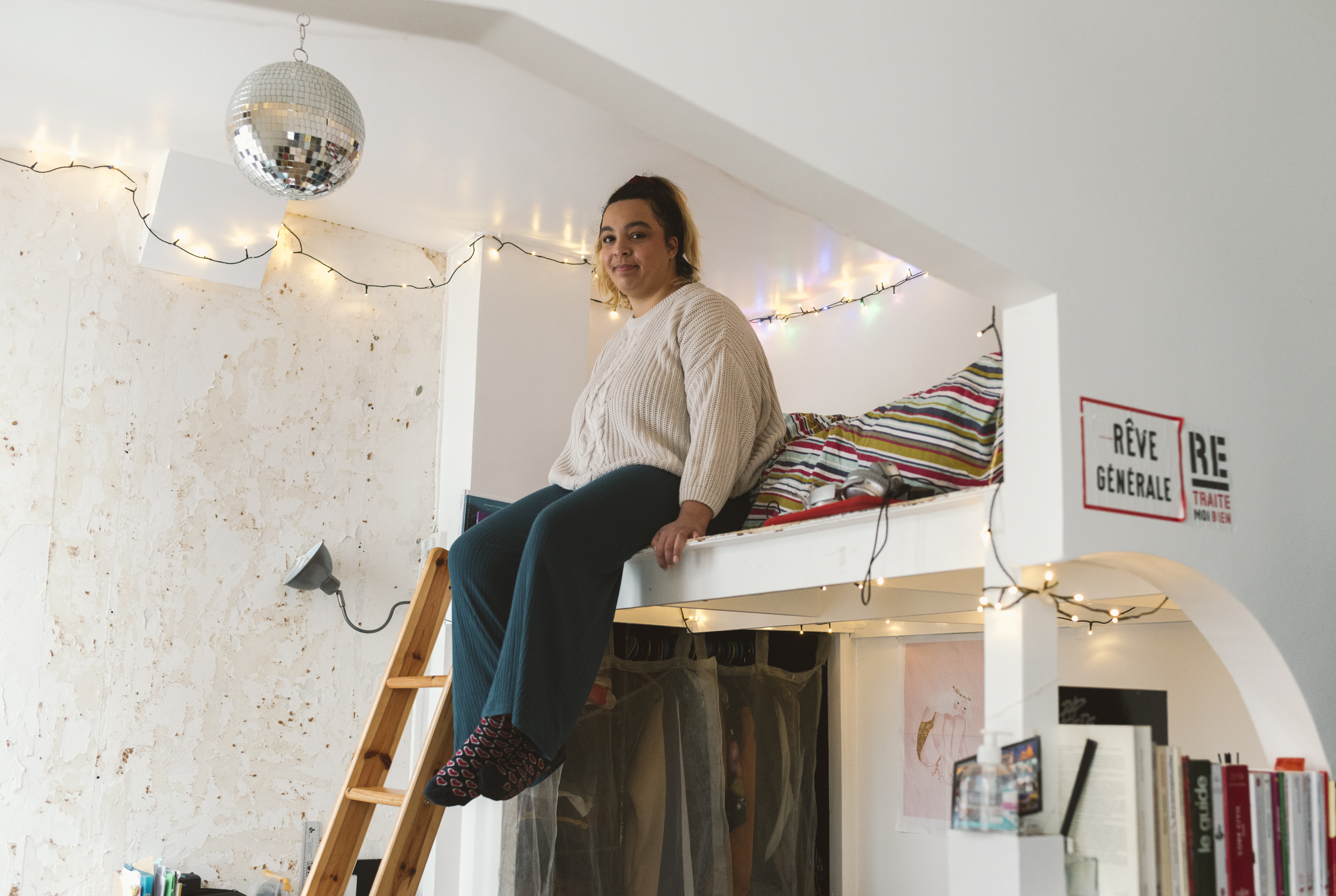 Lénora sitting on her mezzanine bed, her legs dangling in the air.