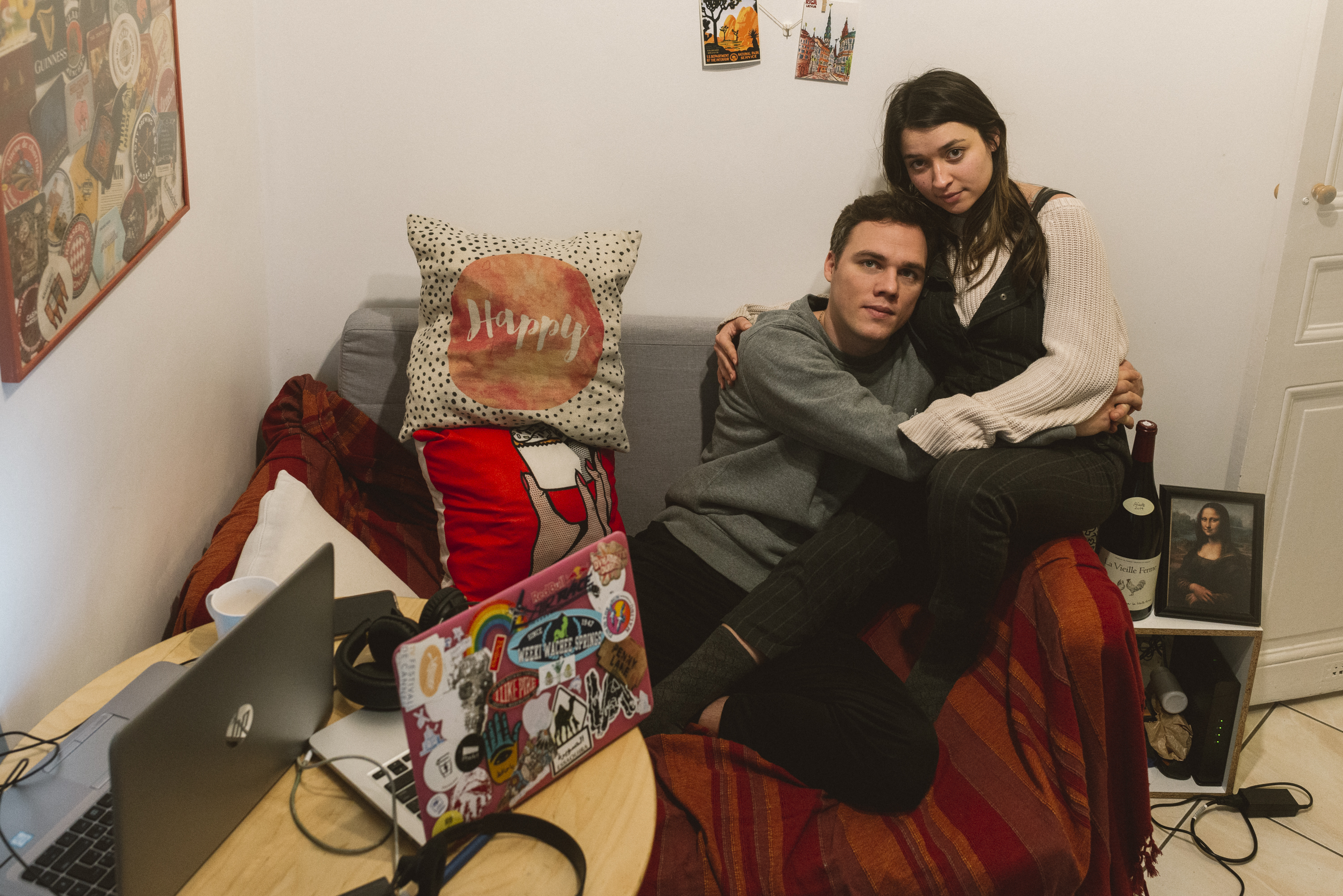 Zoey and Alexandre, hugging on their tiny couch, their laptops piled on top of each other.