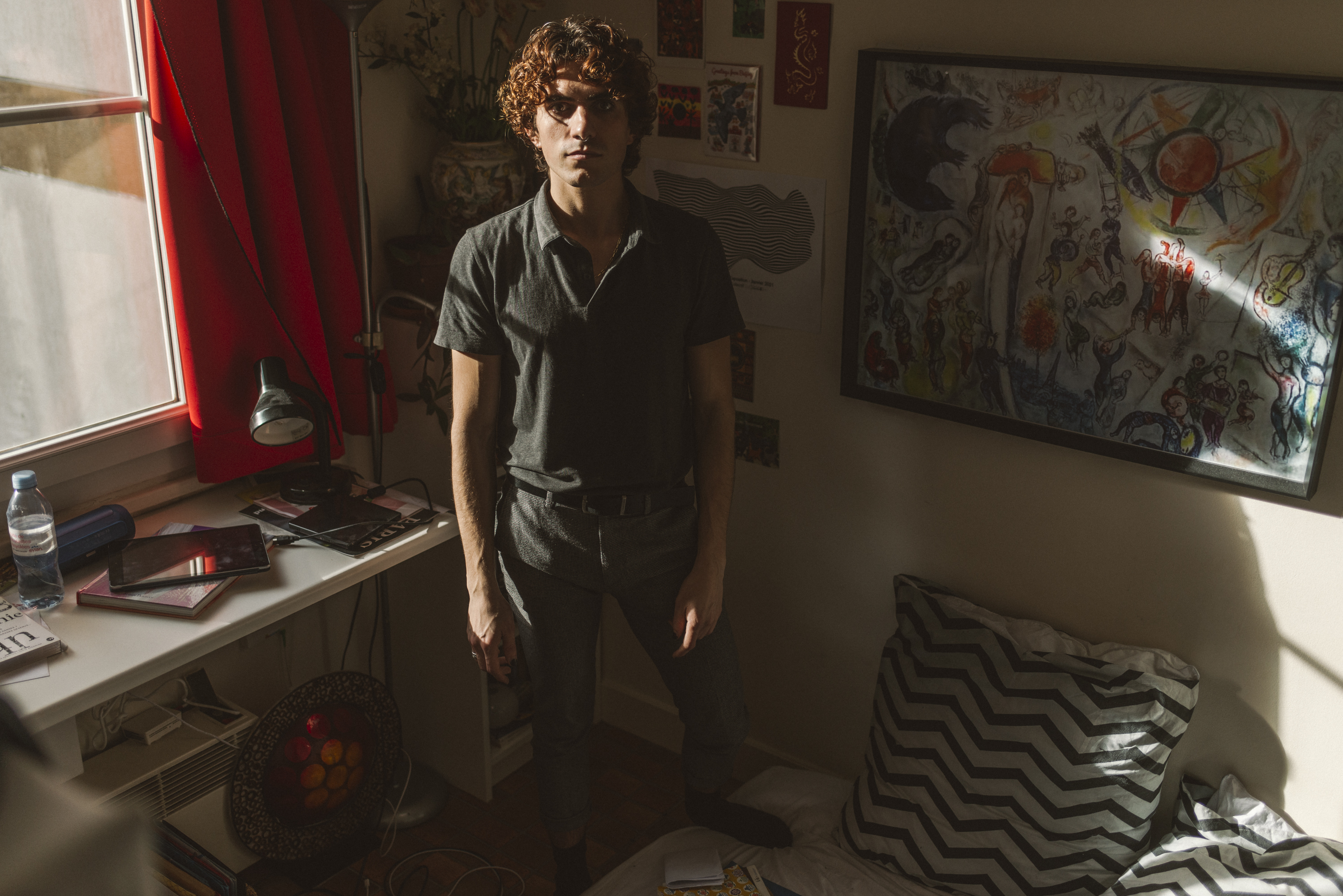 Xavier standing in his cramped flat with one foot on his mattress on the floor.