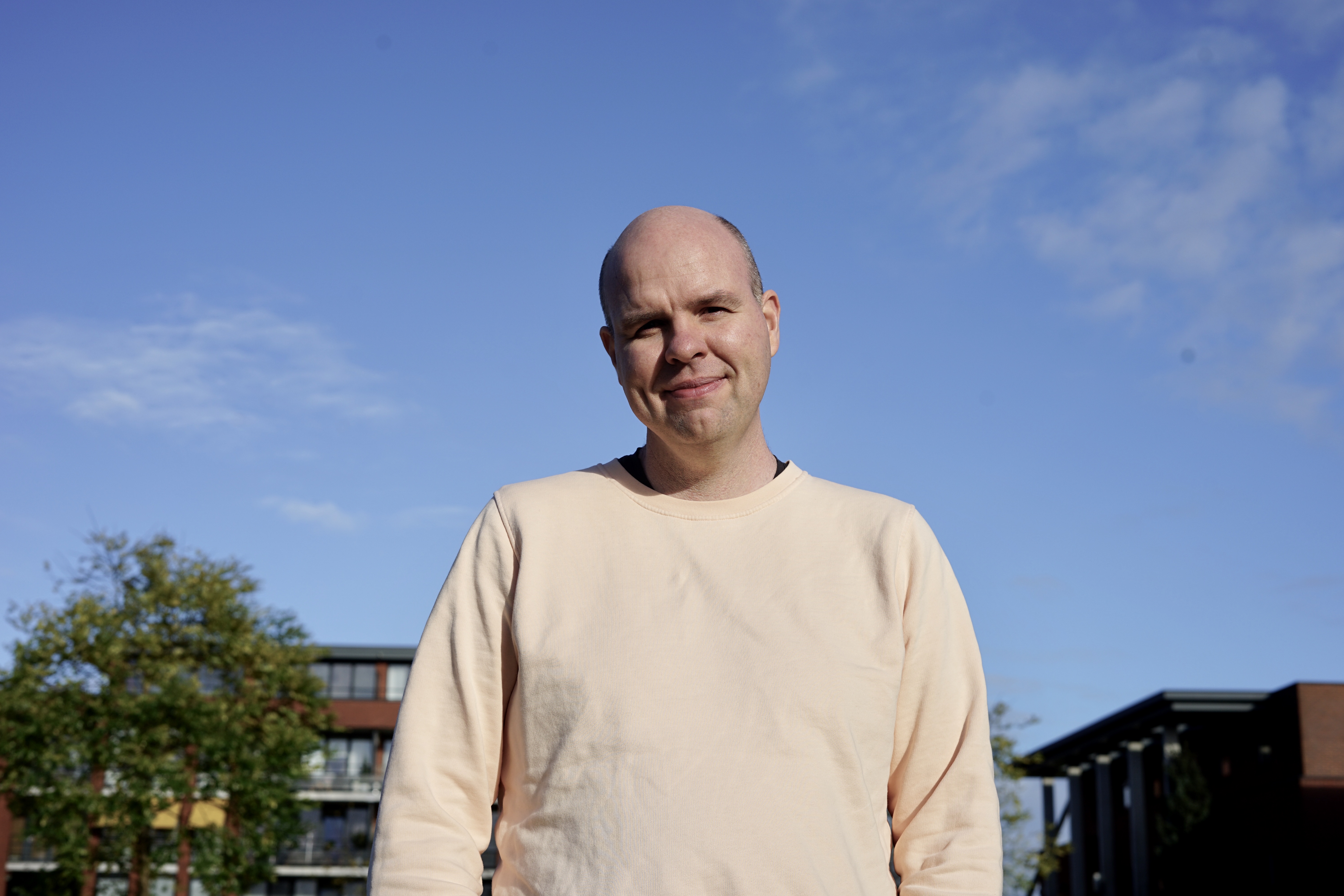 Aart. Male-presenting person, bald with no facial hair, wearing a peach-coloured sweater.