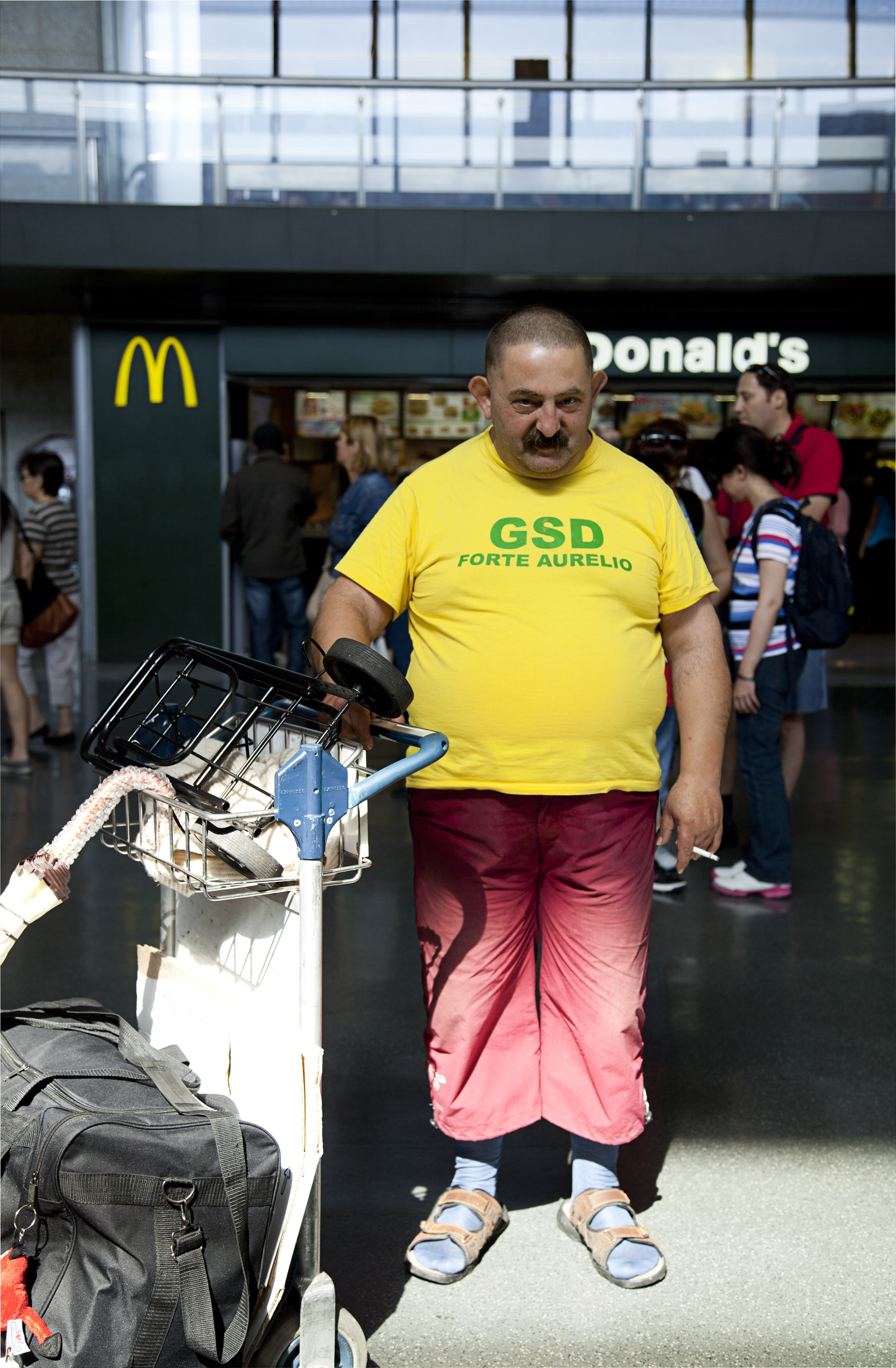 Ein Mann mit Schnurrbart und einem Trolley voller Gepäck posiert im Hauptbahnhof Roms für ein Foto