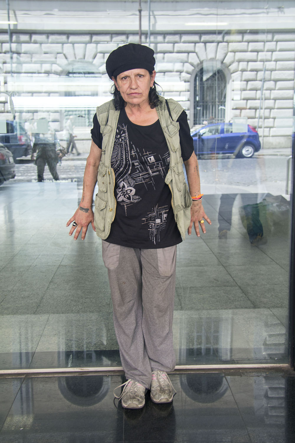 Eine Frau in dunklem T-Shirt, Weste, Jogginghose und dreckigen Sneakern posiert am Hauptbahnhof Roms für ein Foto