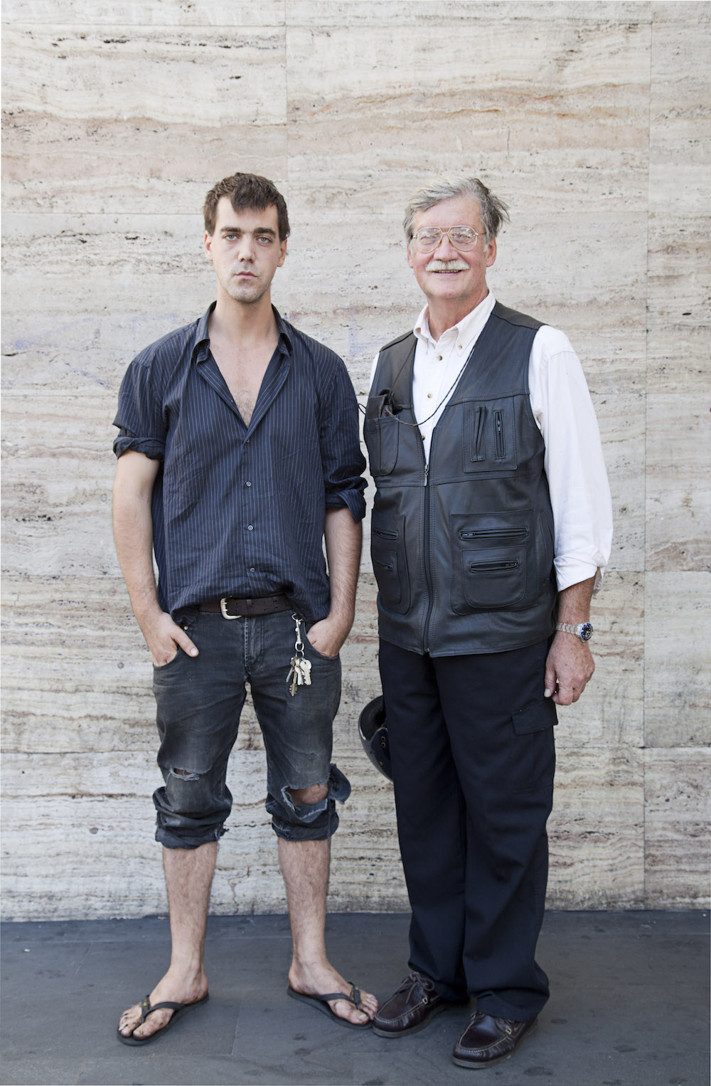Ein ernst dreinblickender junger Mann in Hemd und hochgekrempelten Jeans posiert mit seinem Vater vor dem Hauptbahnhof Roms für ein Foto