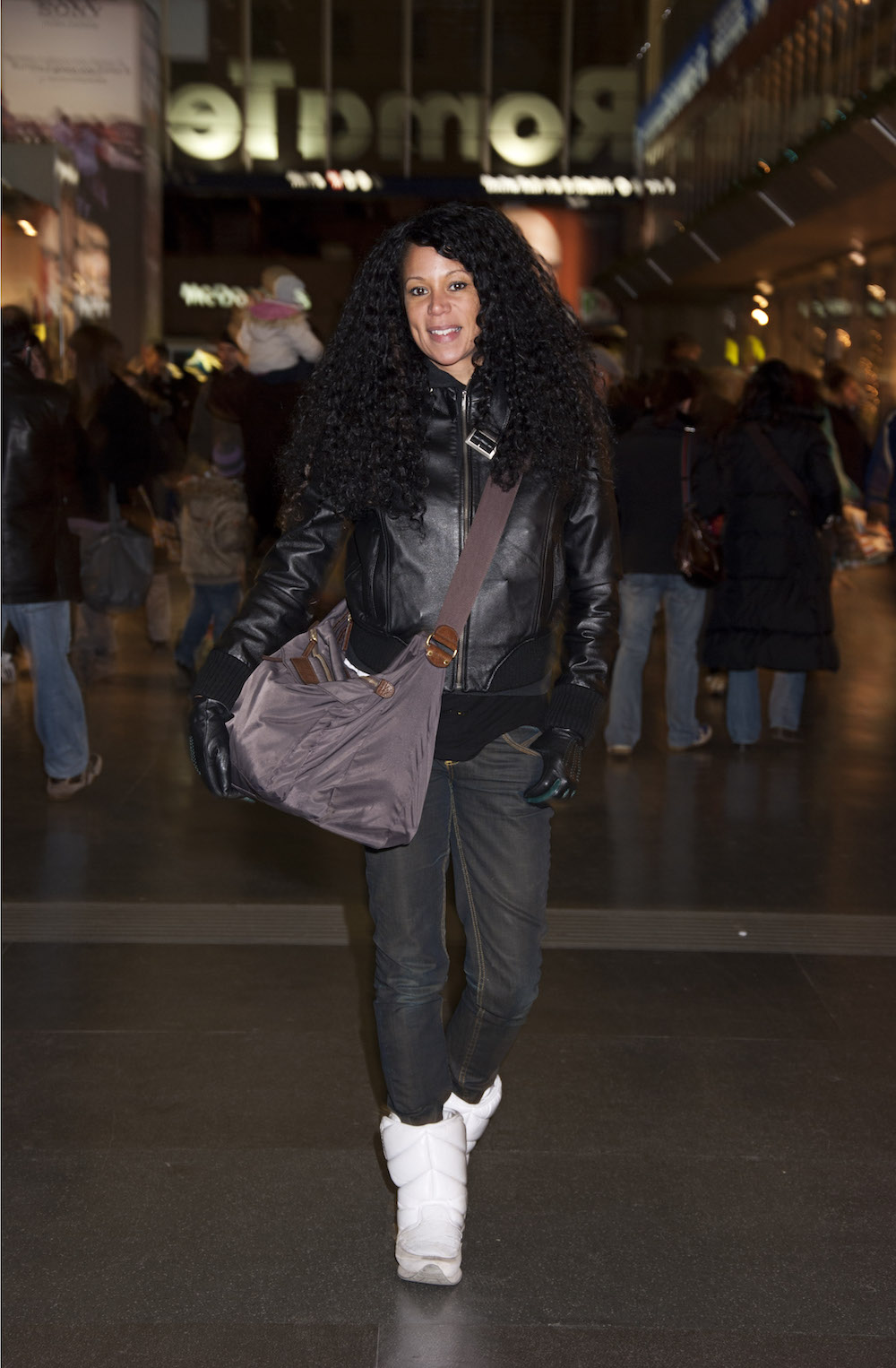 Eine junge Frau mit dunklen Locken und einer großen Tasche posiert im Hauptbahnhof Roms für ein Foto