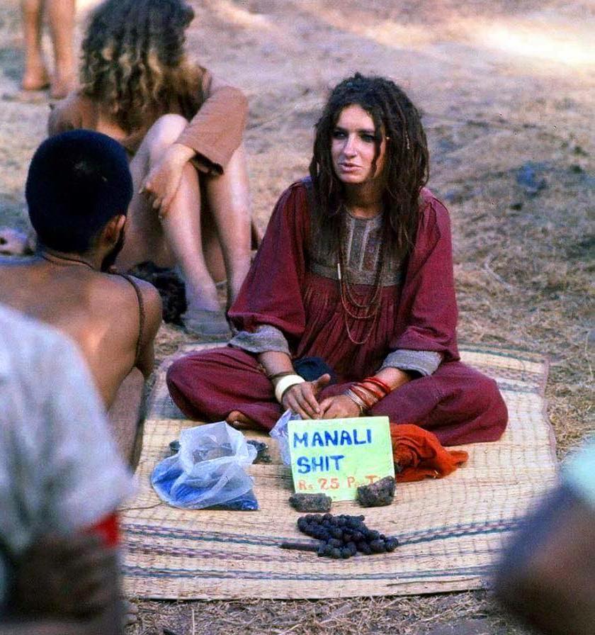 Eine Frau mit Dreadlocks sitzt auf einer Matte, vor ihr ein Schild mit der Aufschrift
