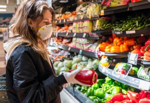 Shopping during a pandemic. A young woman wearing protective mask and gloves shopping vegetable in a store.