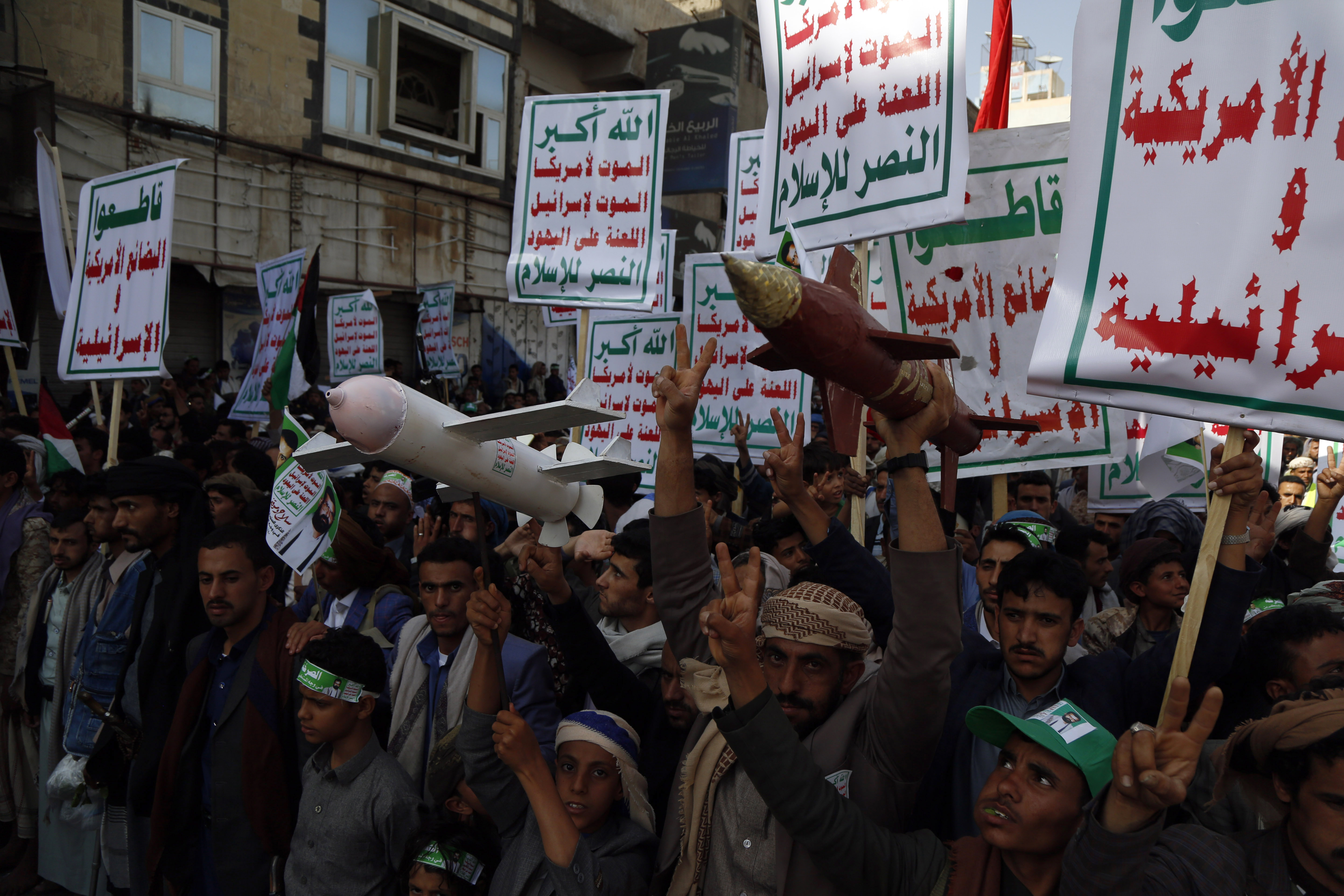 People hold signs and drone replicas while protesting.