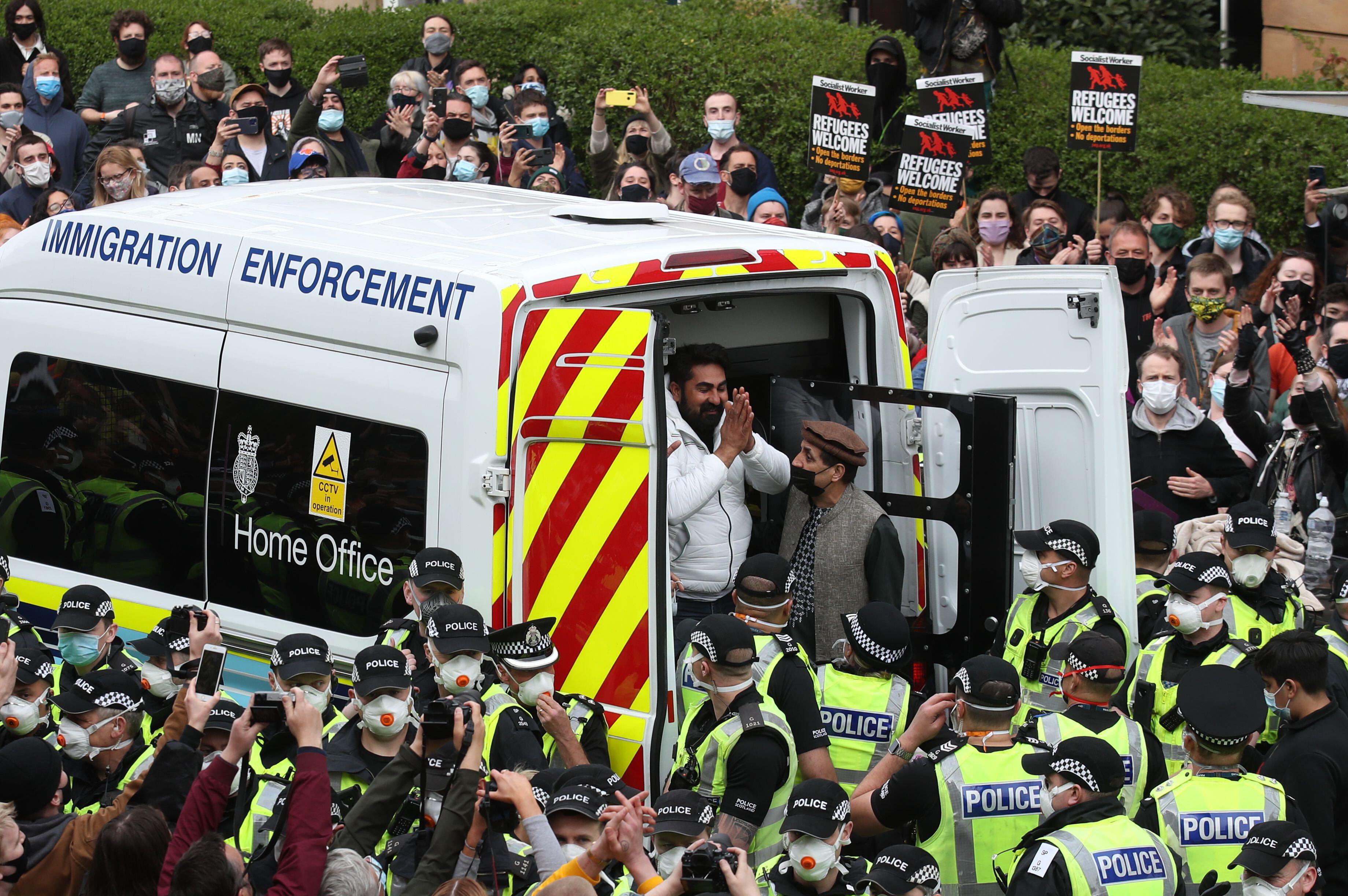 One of two men are released from the back of an Immigration Enforcement van accompanied by Mohammad Asif, director of the Afghan Human Rights Foundation, in Kenmure Street, Glasgow which is surrounded by protesters. Photo: PA Images / Alamy Stock Photo
