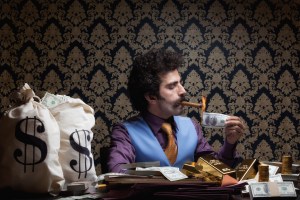 ​Adult man lighting cigar with burnt dollar bill.