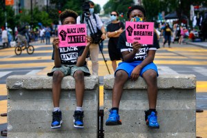 Tyshawn, 9, left, and his brother Tyler, 11, right, of Baltimore, hold signs saying "Black Lives Matter" and "I Can't Breathe" as they sit on a concrete barrier near a police line as demonstrators protest on Wednesday, June 24, 2020, in Washington.