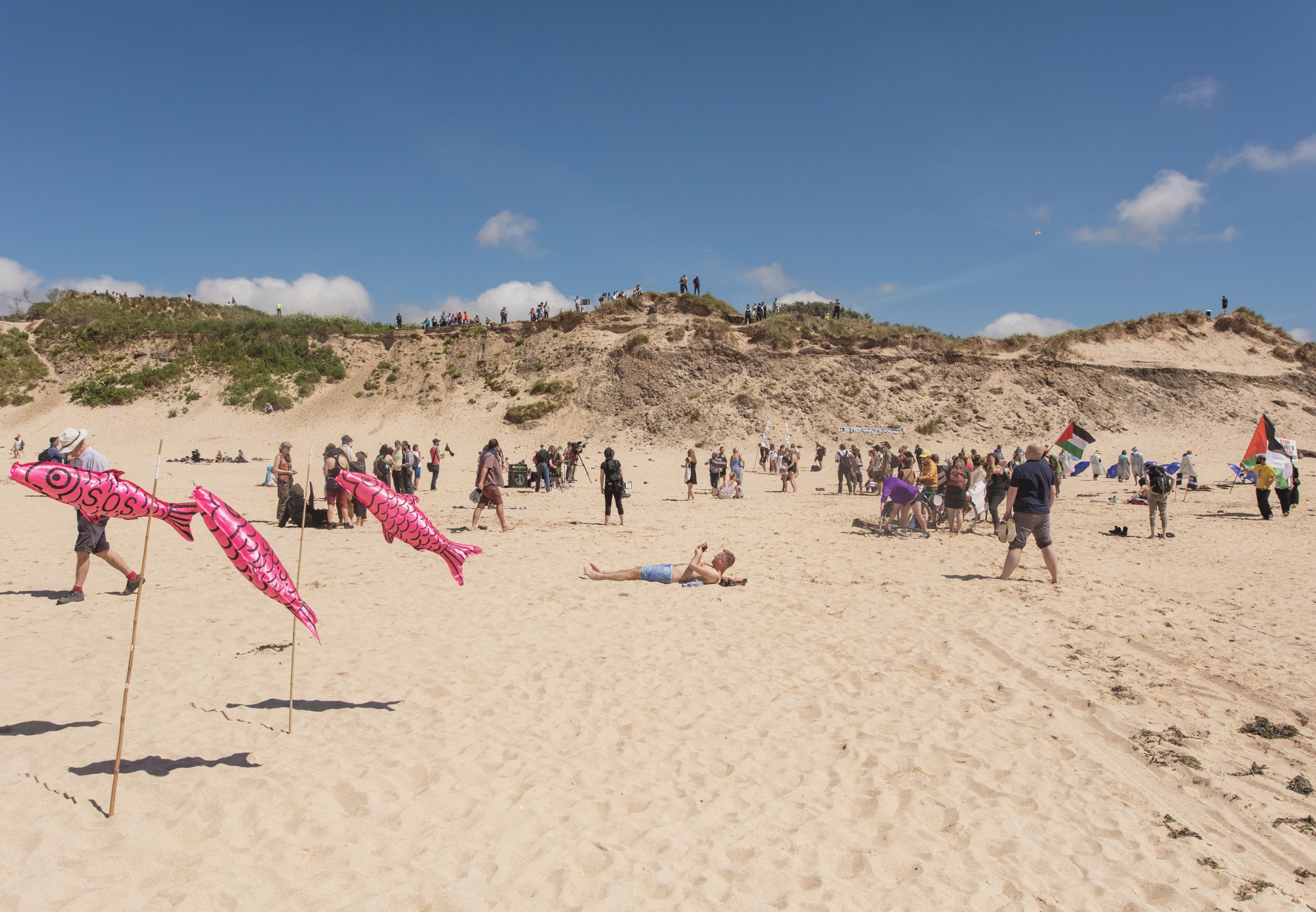 A man relaxes on the beach as he is surrounded by protesters carrying Palestinian flags and placards.